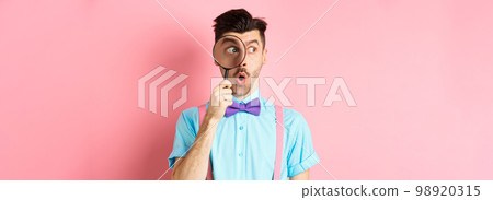 Surprised man saying wow and look aside through magnifying glass, checking out promo offer, standing over pink background Surprised man saying wow and look aside through magnifying glass, checking out promo offer, standing over pink background 98920315
