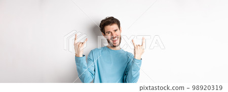 Excited handsome man celebrating, having fun and showing rock on horns gesture, enjoing party, smiling at camera, standing on white background Excited handsome man celebrating, having fun and showing rock on horns gesture, enjoing party, smiling at camera, standing on white background 98920319