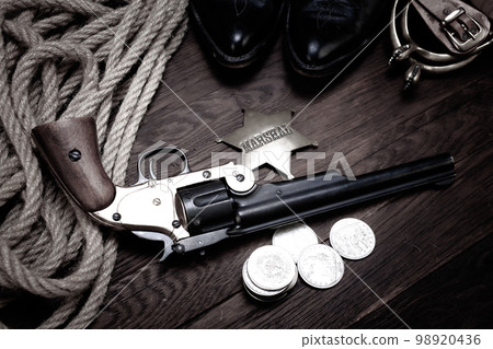 Old West revolver with U.S. Marshal badge and silver dollars with hat, rope and cowboy boots Old West revolver with U.S. Marshal badge and silver dollars with hat, rope and cowboy boots 98920436