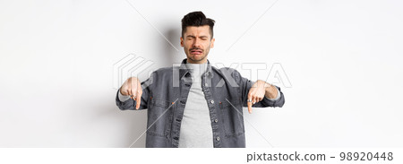 Sad crying man whining, pointing fingers down disappointed, showing bad news, standing upset on white background 98920448