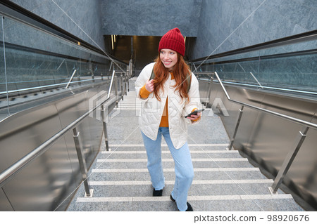 Outdoor shot of young woman plans route, follows map on smartphone app, goes up stairs with backpack and smiles 98920676