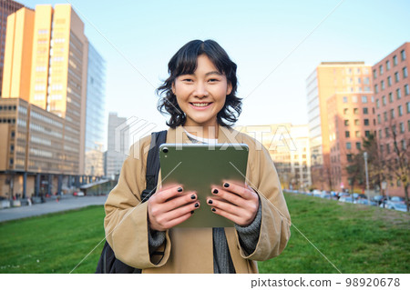 Happy young brunette girl, asian woman walks around city with tablet, goes to university with her digital gadget and backpack 98920678