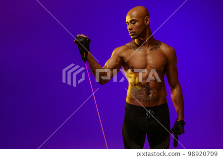 Sporty man with naked torso performs exercises with expander on studio background Sporty man with naked torso performs exercises with expander on studio background 98920709
