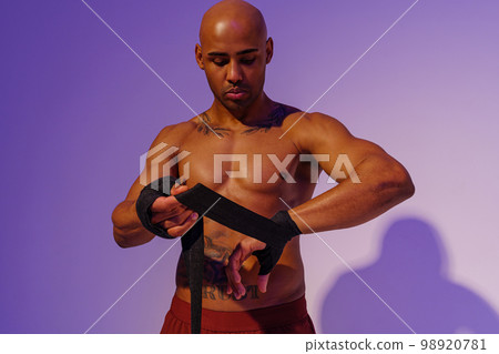 Sporty man with naked torso taping his arms with bandage before fight on studio background Sporty man with naked torso taping his arms with bandage before fight on studio background 98920781