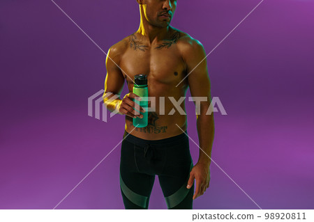 Close up of sporty man with muscled naked torso holding bottle with water on studio background Close up of sporty man with muscled naked torso holding bottle with water on studio background 98920811
