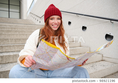 Beautiful girl tourist sits on stairs with city map, plans her journey, looks for direction while travelling around town, searches route for sightseeing Beautiful girl tourist sits on stairs with city map, plans her journey, looks for direction while travelling around town, searches route for sightseeing 98921196
