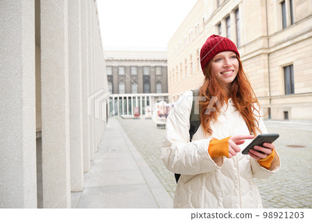 Beautiful smiling girl, tourist with backpack, holding smartphone, using map on mobile phone application, looking for sightseeing in internet app, standing outdoors Beautiful smiling girl, tourist with backpack, holding smartphone, using map on mobile phone application, looking for sightseeing in internet app, standing outdoors 98921203