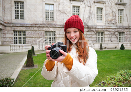 Happy redhead girl tourist, takes photos, photographer with professional camera walks around city and captures beautiful pictures 98921285