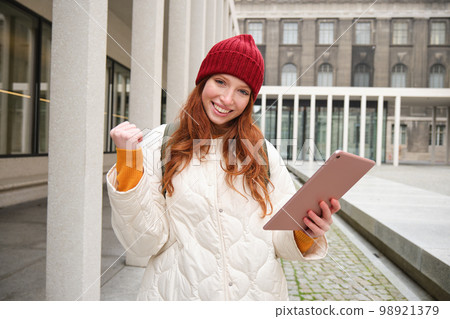 Stylish ginger girl, tourist walks with digital tablet around city, woman connects to iternet on her gadget, looking up information, texting message 98921379