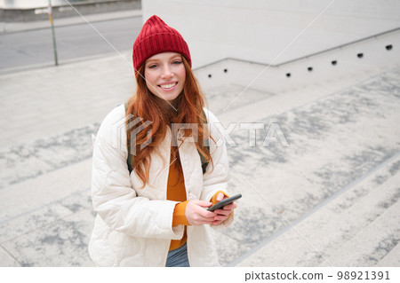 Smiling redhead girl, student tourist walks around city, goes up the stairs, looks at mobile phone map to get around town, sends message on smartphone Smiling redhead girl, student tourist walks around city, goes up the stairs, looks at mobile phone map to get around town, sends message on smartphone 98921391