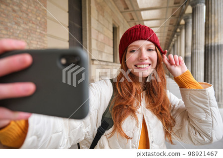 Cute young redhead woman takes selfie on street with mobile phone, makes a photo of herself with smartphone app on street 98921467