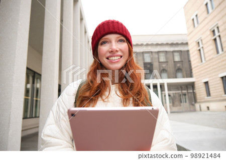 Stylish ginger girl, tourist walks with digital tablet around city, woman connects to iternet on her gadget, looking up information, texting message 98921484