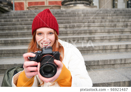 Young student, photographer sits on street stairs and checks her shots on professional camera, taking photos outdoors Young student, photographer sits on street stairs and checks her shots on professional camera, taking photos outdoors 98921487