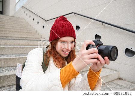 Urban people and lifestyle. Happy redhead woman takes photos, holding professional digital camera, photographing on streets Urban people and lifestyle. Happy redhead woman takes photos, holding professional digital camera, photographing on streets 98921992