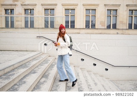 Joyful girl tourist looks at mobile phone, texts message on smartphone social media application, walks around city, looks for sightseeing on mobile app 98922102