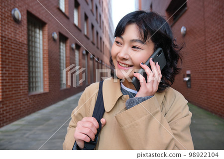 Portrait of young korean woman walking down street with phone, talking with someone, makes a call, has telephone conversation Portrait of young korean woman walking down street with phone, talking with someone, makes a call, has telephone conversation 98922104