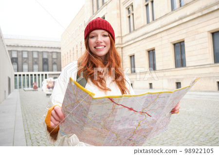 Beautiful redhead woman, tourist with city map, explores sightseeing historical landmark, walking around old town, smiling happily Beautiful redhead woman, tourist with city map, explores sightseeing historical landmark, walking around old town, smiling happily 98922105