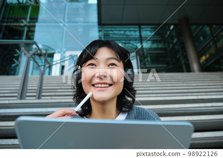 Close up of smiling asian girl feels inspired while draws on digital tablet, makes graphic design project, pencils user interface assignment, sits on stairs near campus Close up of smiling asian girl feels inspired while draws on digital tablet, makes graphic design project, pencils user interface assignment, sits on stairs near campus 98922126