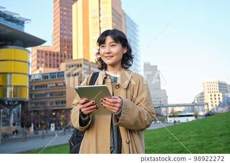 Happy young brunette girl, asian woman walks around city with tablet, goes to university with her digital gadget and backpack Happy young brunette girl, asian woman walks around city with tablet, goes to university with her digital gadget and backpack 98922272