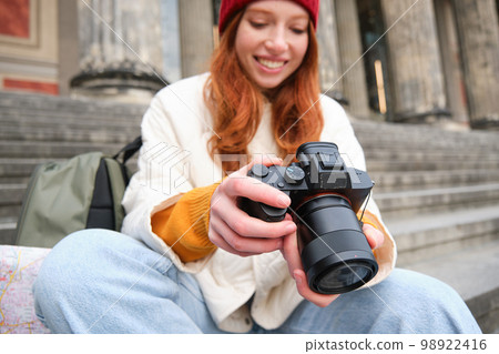 Young student, photographer sits on street stairs and checks her shots on professional camera, taking photos outdoors Young student, photographer sits on street stairs and checks her shots on professional camera, taking photos outdoors 98922416