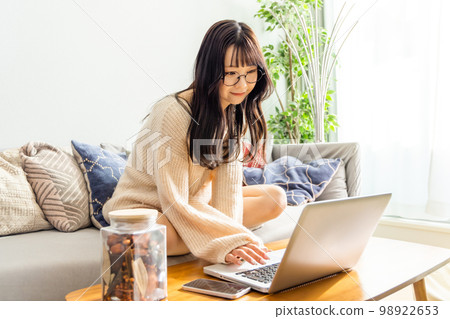 A woman sitting cross-legged on a sofa and using a laptop A woman sitting cross-legged on a sofa and using a laptop 98922653