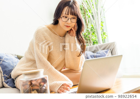 A woman sitting cross-legged on a sofa and using a laptop 98922654