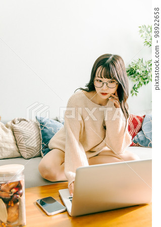 一位女士盤腿坐在沙發上,使用筆記本電腦 一位女士盤腿坐在沙發上,使用筆記本電腦 98922658