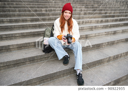 Young student, photographer sits on street stairs and checks her shots on professional camera, taking photos outdoors Young student, photographer sits on street stairs and checks her shots on professional camera, taking photos outdoors 98922935