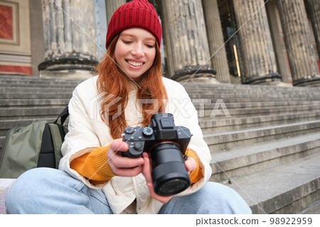 Portrait of young photographer girl, sits on stairs with professional camera, takes photos outdoors, making lifestyle shooting 98922959