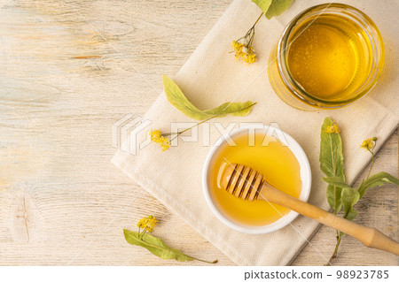 Honey bee in glass jar and bowl with linden flower with honey dipper on wooden background. 98923785