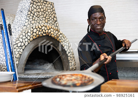 Positive man chef preparing pizza in pizzeria Positive man chef preparing pizza in pizzeria 98925161