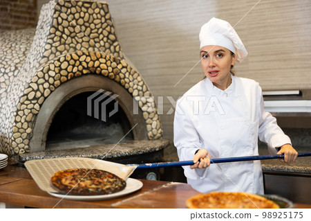 Stressed woman chef preparing pizza in pizzeria Stressed woman chef preparing pizza in pizzeria 98925175