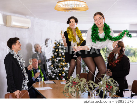 Excited girls dancing on table during New Year corporate party Excited girls dancing on table during New Year corporate party 98925176