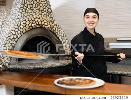 Smiling woman chef preparing pizza in restaurant Smiling woman chef preparing pizza in restaurant 98925229