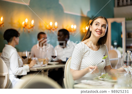 Positive young woman eating salad and drinking red wine in cozy restaurant Positive young woman eating salad and drinking red wine in cozy restaurant 98925231