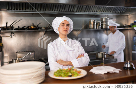 Portrait of female chef with crossed arms along with team of cooks in kitchen of restaurant Portrait of female chef with crossed arms along with team of cooks in kitchen of restaurant 98925336
