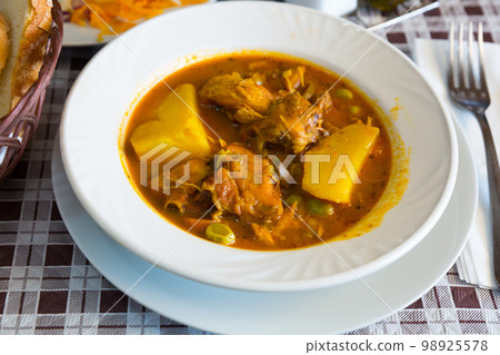 Close up of stewed chicken with red sauce, potatoes and vegetables at plate 98925578