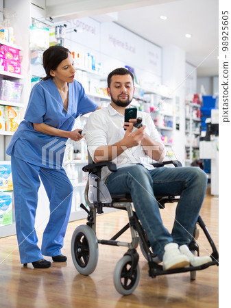 Female pharmacist advising disabled man in drugstore 98925605