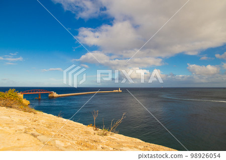 Valetta, Malta - 12 16 22: sea view to Pont Sant Elmo bridge and lighthouse in sunny weather with dramatic sky Valetta, Malta - 12 16 22: sea view to Pont Sant Elmo bridge and lighthouse in sunny weather with dramatic sky 98926054