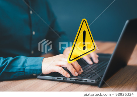 Adult man using computer laptop with triangle caution warning sign for notification error. Computer virus detected, personal data protection, network security and maintenance concept. Adult man using computer laptop with triangle caution warning sign for notification error. Computer virus detected, personal data protection, network security and maintenance concept. 98926324