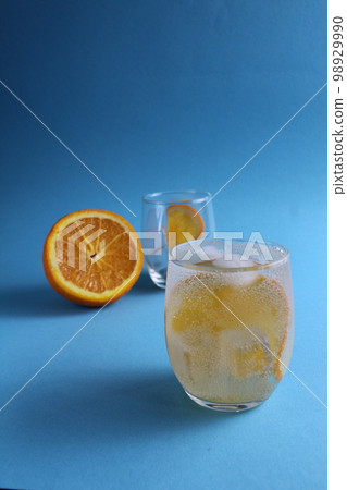 Step-by-step making of lemonade. Step 2. Pour the fruit orange with soda water. A glass of lemonade orange on a blue background with a place for text . close-up Step-by-step making of lemonade. Step 2. Pour the fruit orange with soda water. A glass of lemonade orange on a blue background with a place for text . close-up 98929990