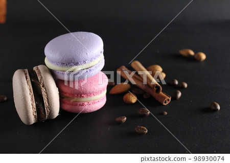 Macaroon and sticks of cinnamon almonds lie next to a black background with a place to text and with a copyspace 98930074
