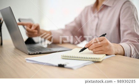 A businesswoman working at her desk, using laptop and taking notes on her notepad. A businesswoman working at her desk, using laptop and taking notes on her notepad. 98930285