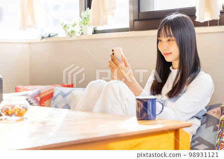 坐在矮沙發上並使用智能手機的年輕女子 坐在矮沙發上並使用智能手機的年輕女子 98931121