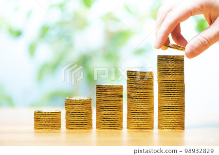 Close-up of a male hand stacking gold coins in a stepped pattern Close-up of a male hand stacking gold coins in a stepped pattern 98932829