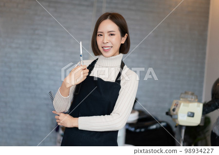 Portrait of a young asian female hairdresser holding qualified haircut tools. 98934227