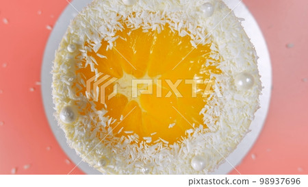 Cake with orange and coconut shavings spun on a pink background. 98937696