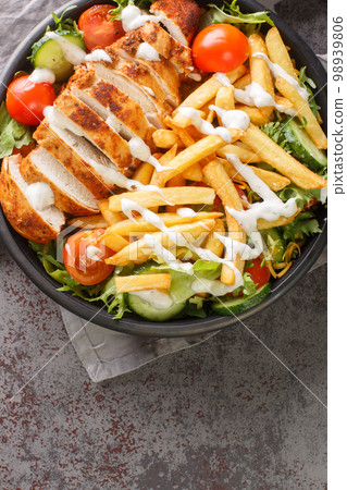 Pittsburgh Chicken Salad slices of juicy chicken breast and a pile of hot, crispy fries on top of a cool, crunchy salad closeup on the bowl. Vertical top view 98939806