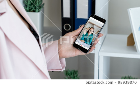 Mobile conference. Video call. Corporate telecommuting. Female business partners discussing work online on phone screen at digital office. Mobile conference. Video call. Corporate telecommuting. Female business partners discussing work online on phone screen at digital office. 98939870