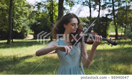 A young girl plays the violin in a city park. Video in motion. 98940047